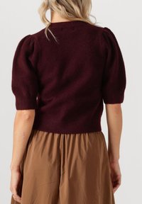 Bordeaux gebreide trui met korte pofmouwen, een geribde zoom, gedragen over een tan geplooide rok met een zachte, gestructureerde afwerking.