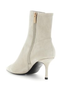 Bottine en suede beige avec fermeture éclair sur le côté, bout pointu et talon aiguille mince de hauteur intermédiaire.