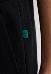 Zwarte gebreide stof met een geribbelde textuur, gekenmerkt door een klein teal label met een logo dat aan de zijkant is geplaatst.