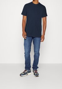 Marinblå crew-neck t-shirt i kombination med blå denimjeans och flerfärgade sneakers med en framträdande logotyp och texturerad mellansula.