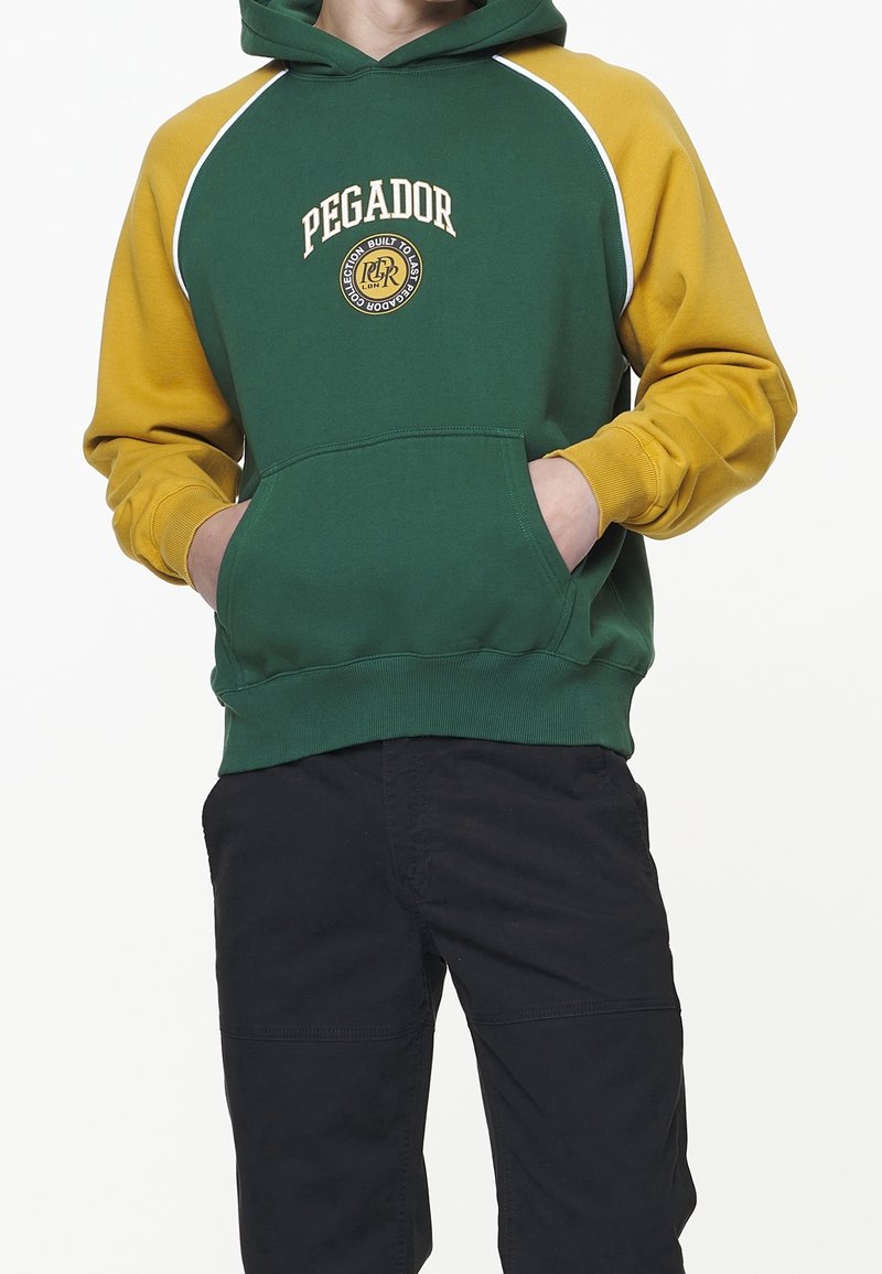 Sweat à capuche vert et jaune avec une poche kangourou, des accents blancs et le logo "PEGADOR". Comprend une capuche à cordon de serrage et un ourlet côtelé.