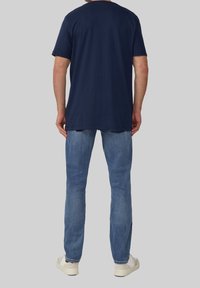 Marineblauwe katoenen t-shirt met korte mouwen, relaxed fit en ronde hals; gecombineerd met lichtblauwe denim jeans en witte sneakers.