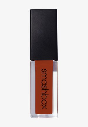 Rouge à lèvres liquide avec un capuchon noir rectangulaire et un emballage transparent. Contient une teinte rouge orangé profond étiquetée "smashbox."