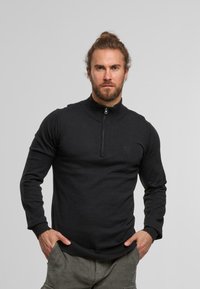 Sudadera negra de media cremallera hecha de tejido de punto. Presenta un cuello alto, mangas largas y puños y dobladillo acanalados. Detalle sutil del logo.