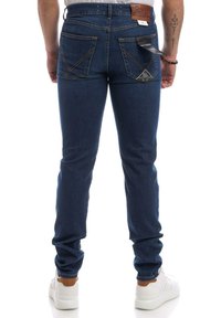 Modré džíny z denimu s úzkým střihem, zadní kapsy zdobené vzorem ve tvaru V a kožená nášivka na pase. Kombinované s bílými teniskami.