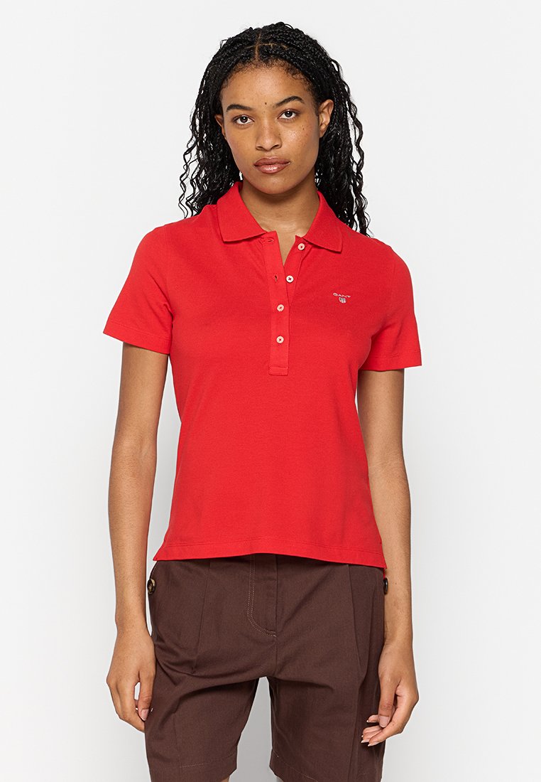 Camiseta polo roja de algodón con mangas cortas, cuello clásico y tapeta de tres botones; presenta un pequeño logo en el pecho.