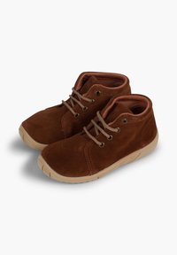 Stivaletti alla caviglia in suede marrone con punta arrotondata, dotati di suola in gomma beige, lacci marroni e occhielli metallici su una superficie liscia.
