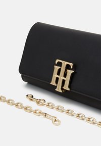 Musta nahkainen clutch-laukku kultaisen logon lukolla, jossa on kullanvärinen ketjuhihna ja sileä pinta. Muoto on suorakulmainen.