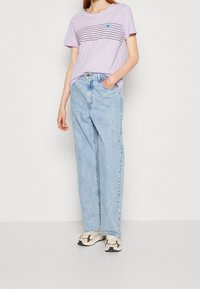 Lyslilla kortærmet t-shirt med horisontale sorte striber og et lille turkist hjerte; parret med lyseblå løstsiddende jeans og mønstrede sneakers.