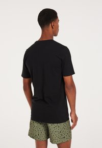 Camiseta negra de manga corta con cuello redondo, combinada con pantalones cortos verdes con un patrón que presenta formas y diseños abstractos en negro.