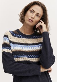 Pull en tricot avec un col rond, une base bleu marine foncé et des rayures horizontales multicolores en bleus, bruns et crème avec des motifs géométriques.