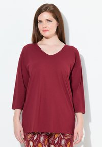 Bordeaux V-hals top met driekwart mouwen, gemaakt van zachte stof. Gecombineerd met gestreepte kastanjebruine en gele broek met bladdesigns.