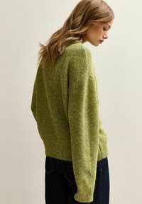 Maglione verde lavorato a maglia con finitura testurizzata, vestibilità ampia, spalle abbassate e maniche lunghe, abbinato a jeans blu scuro.