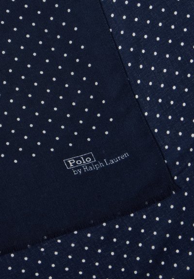Tengerészkék anyag fehér pöttyökkel, amelyen a "Polo by Ralph Lauren" felirat található. A textúra simának és szövöttnek tűnik.