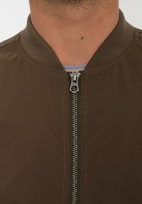 Brązowa kurtka typu bomber z prą�żkowanym kołnierzem i srebrnym zamkiem. Tkanina ma gładką strukturę z widocznym szwem i schludnym designem.