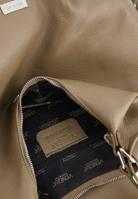 Beige leren handtas interieur met een geprofileerde afwerking, zilveren rits en logodetails op een donkere stofvoering.
