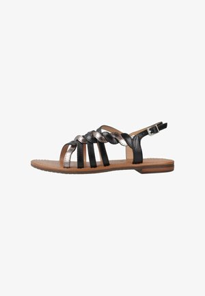 Sandali neri e metallici con cinturini, caratterizzati da un design intrecciato, una suola piatta e una cinghia alla caviglia regolabile, con una texture liscia e dettagli minimi.