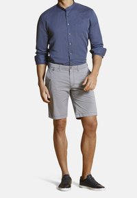 Chemise en lin bleue pour homme avec un col Mandarin, shorts gris à motifs, et baskets noires à semelles blanches. Design boutonné et semi-ajusté.