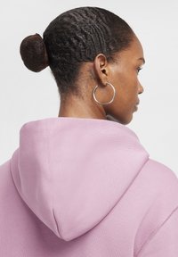 Roza jopa s kapuco z teksturirano površino, z veliko kapuco in vidnim šivanjem. Model nosi uhane v obliki obroča in ima teksturirano pričesko.