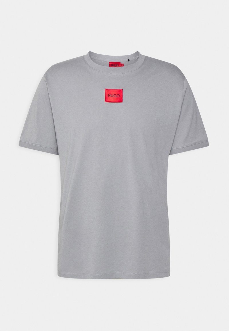 Camiseta de algodón gris con escote redondo, mangas cortas y un parche cuadrado rojo con la inscripción "HUGO" en la parte izquierda del pecho.