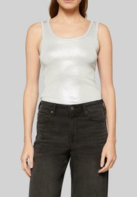 Silver metallic sleeveless tank top with a scoop neckline, fitted design, and smooth texture. Paired with dark, high-waisted jeans.