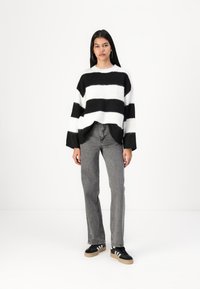 Black and white striped sweater with a loose fit, rounded neckline, and wide sleeves, paired with gray jeans and black sneakers.