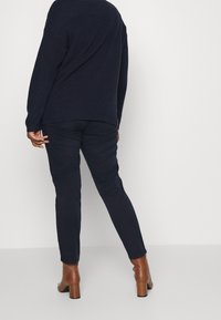 Navy knit sweater with ribbed texture, paired with fitted navy pants. The outfit is complemented by brown heeled ankle boots.