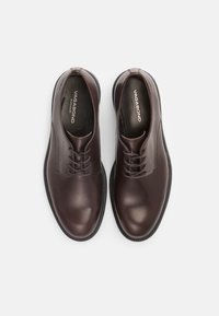 Chaussures habillées en cuir marron foncé avec une finition lisse, un bout rond et un design à lacets. Présentent un logo sur la semelle intérieure et une semelle en caoutchouc texturée.