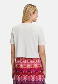 Korte mouwen, cropped top in lichtgrijs met een subtiele glans. Draag het over een kleurrijke, gemusterde rok met geometrische ontwerpen in roze en rood.