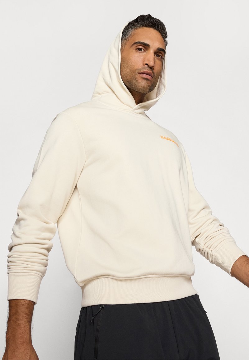 Cremefarbener Hoodie mit einer Kängurutasche. Verfügt über gerippte Bündchen und Saum. Kleinere orangefarbene Branding auf der Brust. Weicher, lockerer Schnitt.