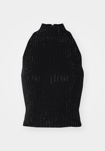 Črn pleteni top z visokim ovratnikom, ki ima rebrasto teksturo in majhne luknjaste vzorce po celotni površini. Zadrga je na hrbtni strani.