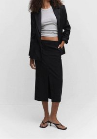 Mustanhattuiset bleiseri päällä harmaa crop-top, yhdistettynä mustaan midi-hameeseen, jossa on etuaukko, ja mustiin flip-flop sandaaleihin.