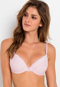 Bra imbottito di pizzo rosa con forma triangolare, delicati motivi floreali, spalline regolabili e un dettaglio centrale a fiocco.