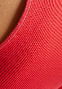 Röd ribbad tyg med en slät yta, med en bred halsringning. Närbild som framhäver färgen och de fina linjerna i materialet.