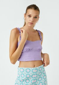 Top corto lavanda con spalline arricciate, caratterizzato da un design aderente e dettagli arricciati sul busto. Abbinato a una gonna con fantasia.