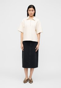 Κρέμ κοντομάνικο πόλο μπλουζάκι με φερμουάρ, μαύρη midi φούστα από τζιν και παπούτσια τύπου slip-on με λεοπάρ μοτίβο. Απλό, άνετο και με μίνιμαλ σχεδιασμό.