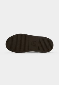 Semelle de chaussure marron foncé avec des rainures horizontales et un petit logo carré au centre, présentée sur un fond blanc uni.