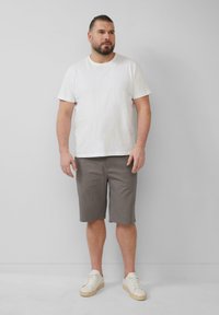 Witte t-shirt met korte mouwen gecombineerd met grijze kniebroekjes en witte sneakers. Eenvoudig ontwerp, casual pasvorm en effen kleuren.