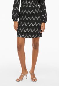 Fustă mini neagră cu model zigzag din fir argintiu, cu talie elastică. Asortată cu sandale argintii cu toc înalt.