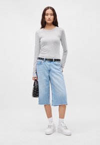 Šedý top s dlhým rukávom, svetlomodré denimo culottes s obratým lemom, čierny cvočkovaný opasok a malá čierna kabelka. Biele tenisky so štrikmi.