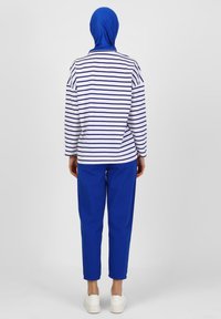 Maglietta a maniche lunghe a righe bianca e blu navy, abbinata a pantaloni blu. Materiale in cotone, vestibilità rilassata, con scarpe da ginnastica bianche visibili in fondo.