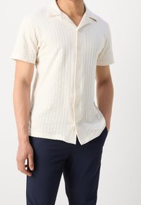 Korte mouwen crème shirt met een textuurpatroon, knoopsluiting aan de voorkant en een zachte stof. Heeft een klassieke kraag en een subtiele zoomafwerking.