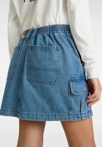 Hame denim dengan warna biru muda, tali pinggang elastik, dua saku samping, dan satu saku flap dengan detail snap perak.