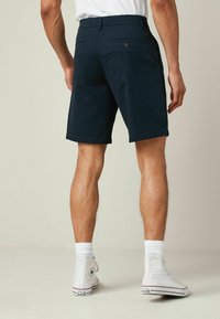 Shorts azul marino con una textura suave, que cuentan con bolsillos traseros y botones marrones. Estilizados con zapatillas blancas de caña alta y calcetines blancos de canalé.