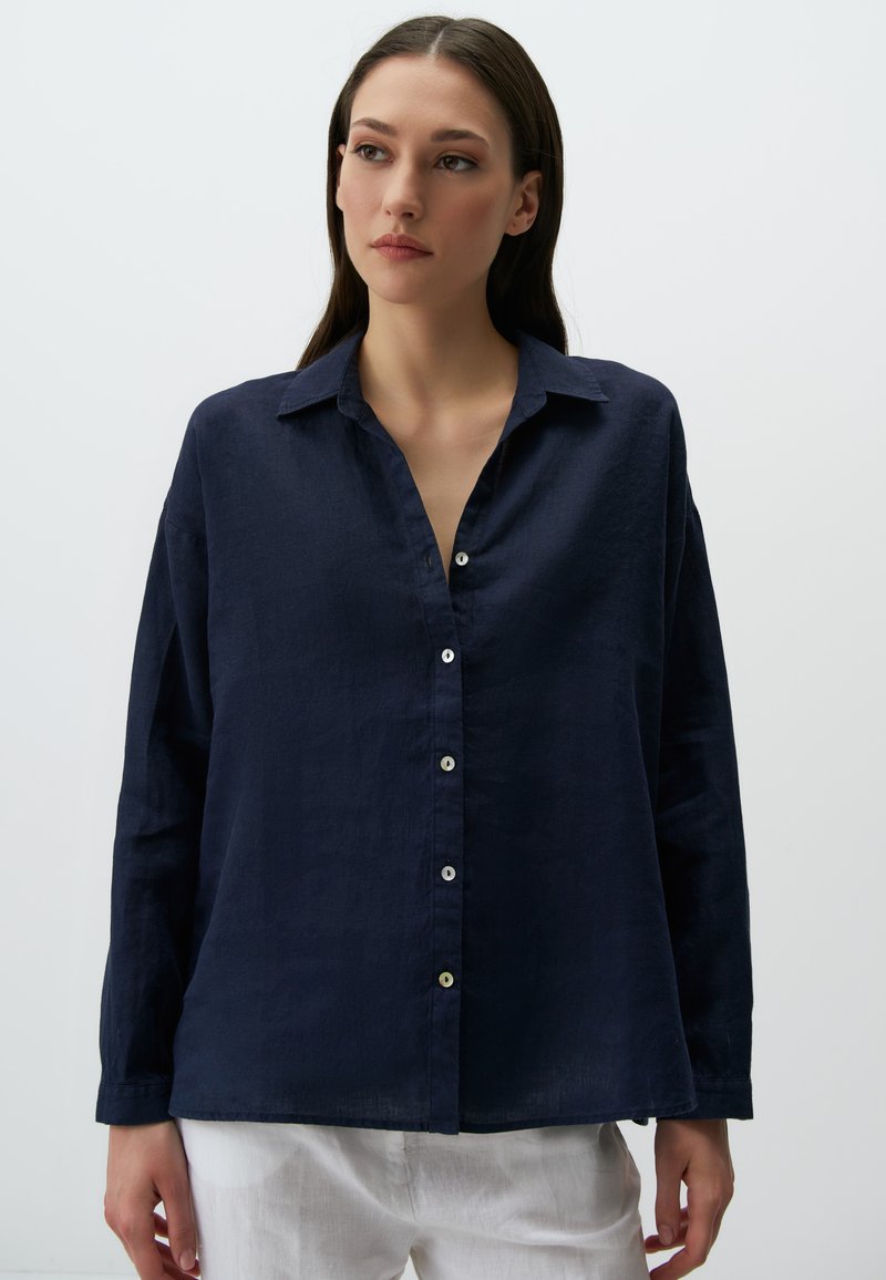 Camicia button-up in lino blu navy con colletto, maniche lunghe e vestibilità comoda. Presenta una patta frontale con bottoni bianchi e una consistenza morbida.