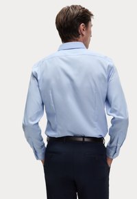 Hellblaues Langarmhemd mit strukturiertem Kragen und Knopfmanschetten, kombiniert mit dunklen Hosen. Glattes Material und figurbetonter Schnitt.