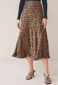 Jupe midi en satin à imprimé léopard, avec un design évasé et une texture légère ; associée à des sandales à talons noirs à lanières.