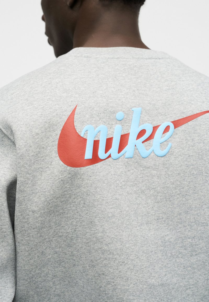 Man wearing gray sweatshirt with large red Nike swoosh and light blue "nike" text on the back, shown from behind.