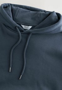 Sweat à capuche oversize gris foncé avec cordons et une étiquette de marque "NEXT" visible à l'intérieur de l'encolure.