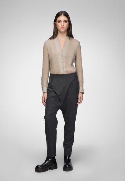 Beige sheer button-up blouse with a v-neck, paired with dark grey tapered trousers featuring a diagonal flap and black chunky boots.